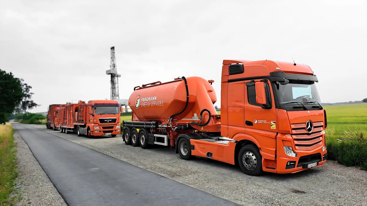 Pumpwagen der Firma Fangmann Energy Services in orange stehen vor einem Bohrturm und einem grünen Feld.