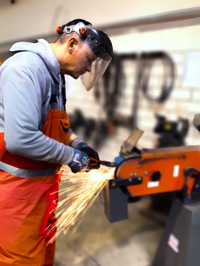 Schlosser arbeitet am Schraubstock mit einer Felx. Es sind Funken zu sehen.